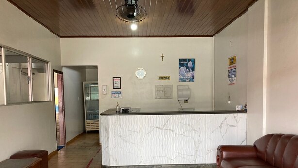 A reception area with a marble counter, a cross on the wall, a clock, and a refrigerator. - Tibiriçá Hotel LTDA (Maraba)