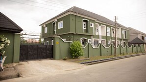 Ein zweistöckiges Haus mit geschlossenem Eingangstor, einem kleinen Garten und einem gepflasterten Auffahrt.