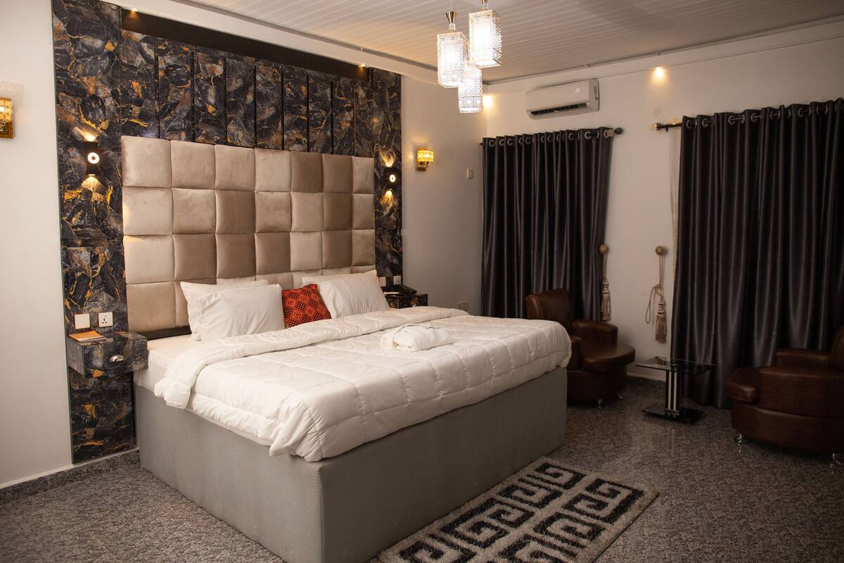 A modern bedroom with a large bed, a marble accent wall, and a chandelier.
