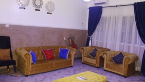Ein Wohnzimmer mit zwei Sofas, einem gelben Hocker und einem schwarzen Sessel.