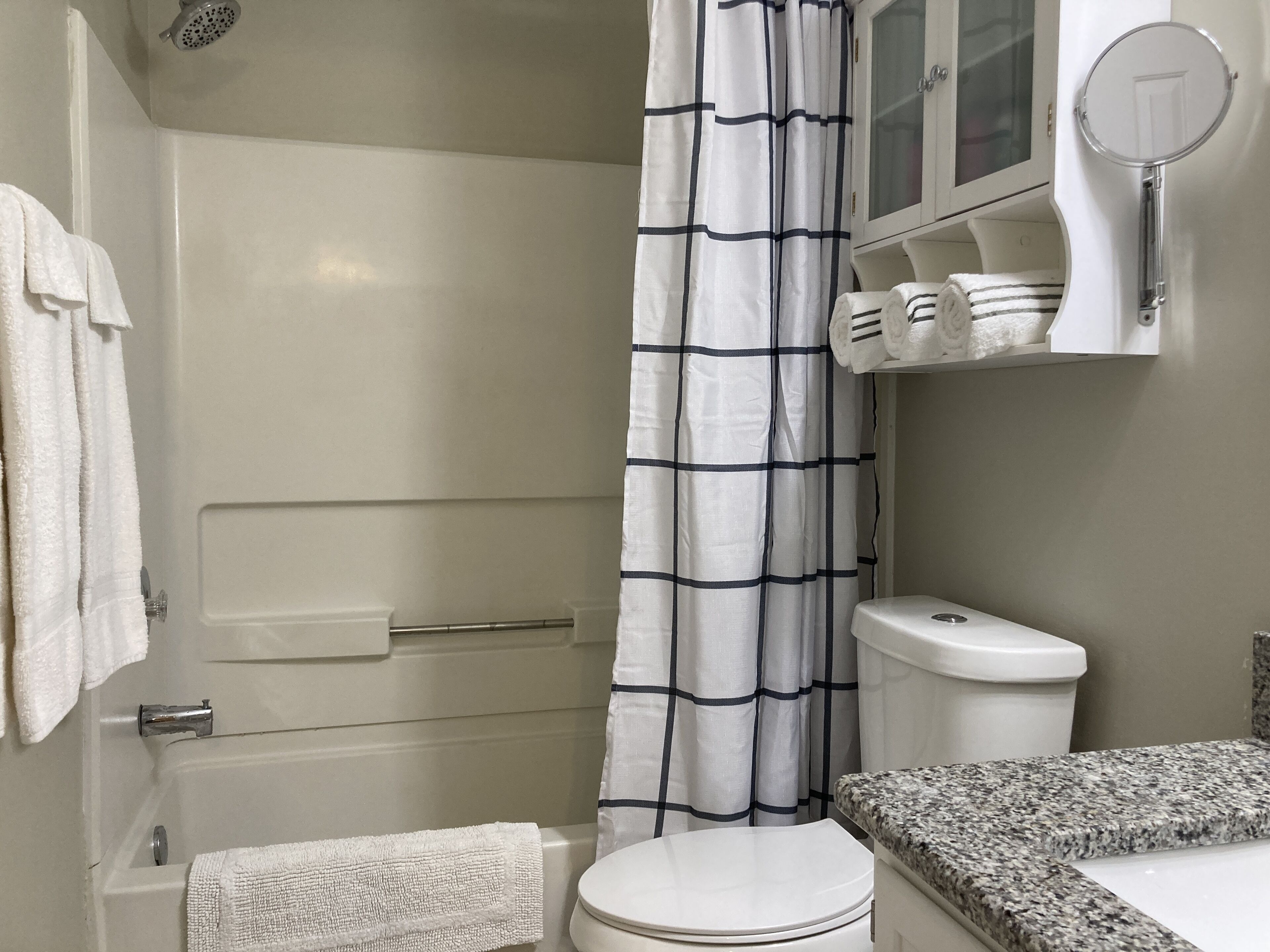 A bathroom with a white bathtub, a white toilet, and a shower curtain with a black grid pattern.
