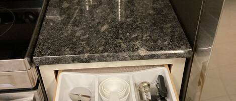 Una cocina con encimera de granito, electrodomésticos de acero inoxidable y un organizador de cajones con utensilios.