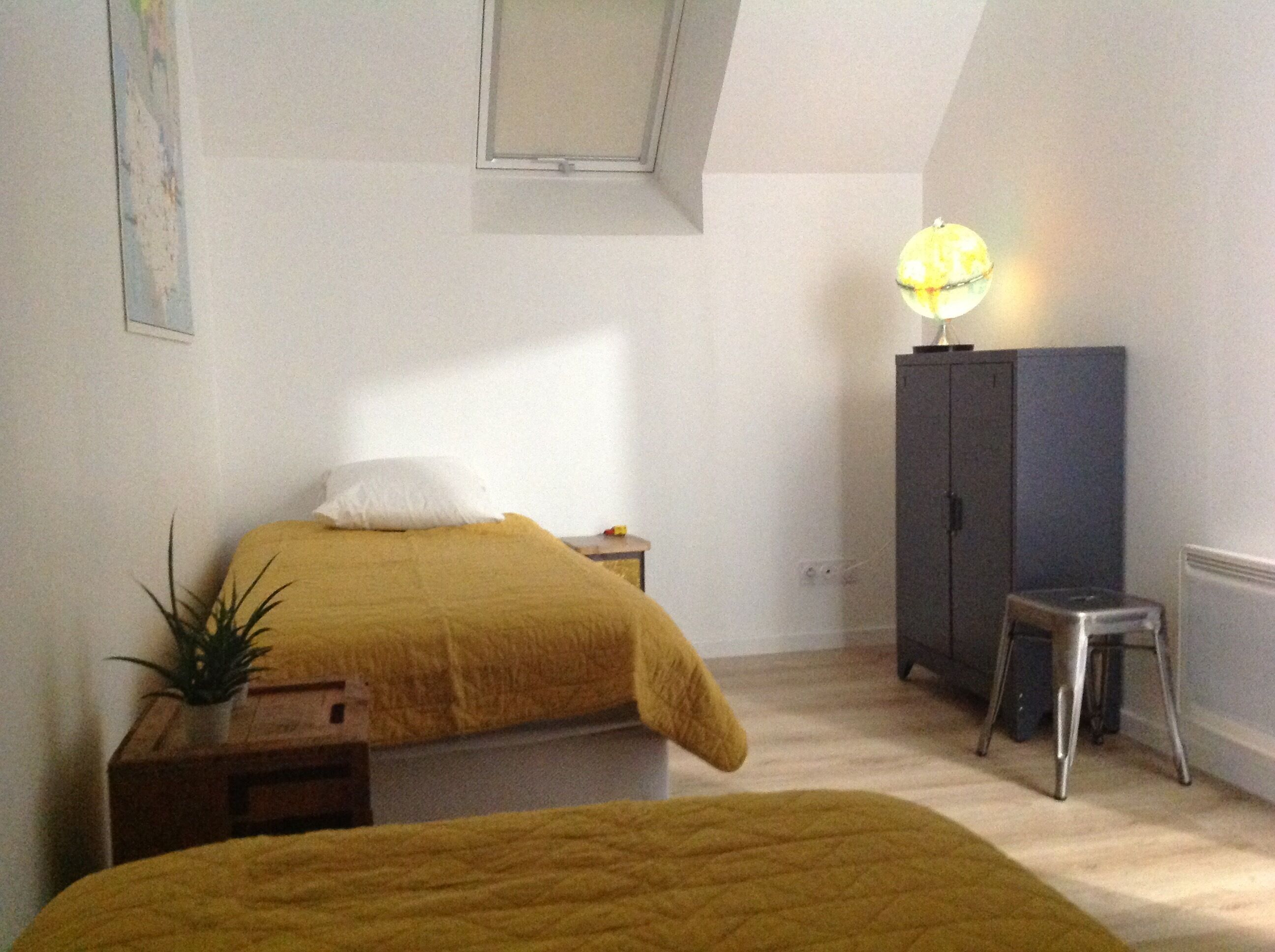A bedroom with a bed, a nightstand, a lamp, a cabinet, and a small stool.