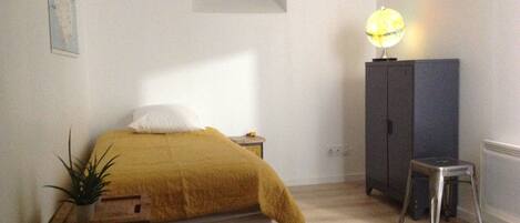 A bedroom with a bed, a nightstand, a lamp, a cabinet, and a small stool.