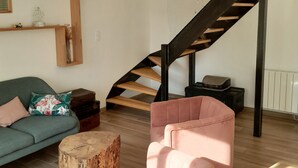 A modern living room with a staircase, a green sofa, pink armchairs, and a wooden coffee table. - The House of Strikes... its Dependency (Le Val-Saint-Père)