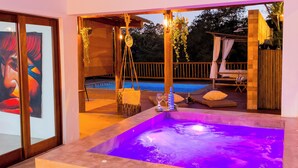 A modern outdoor living area with a hot tub, wooden deck, and a view of a swimming pool.