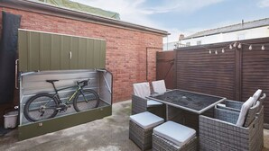 Eine Terrassenfläche mit Tisch und Stühlen, ein Fahrrad in einem Stauraum und eine Backsteinmauer.