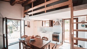 Una cocina con vigas de madera, un comedor con mesa y sillas, y una vista por la puerta abierta.