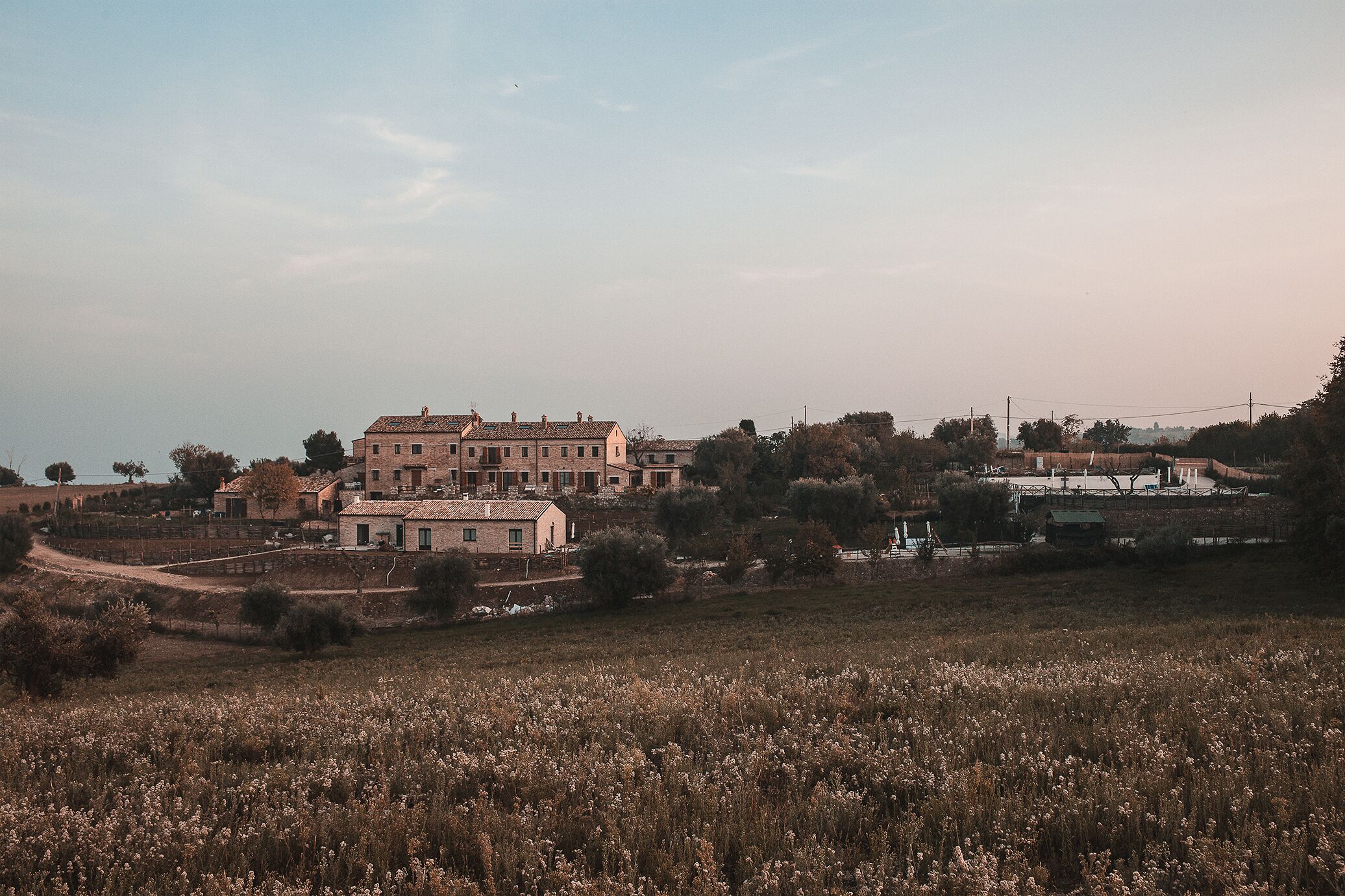 A large, multi-story building with a traditional architectural style, surrounded by a field and some trees.