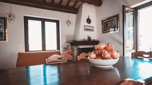 Una mesa de comedor con un cuenco de higos chumbos, sillas de madera, una chimenea y una ventana con vistas.