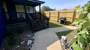 Un patio trasero residencial con un porche cubierto, una parrilla y una valla de madera.