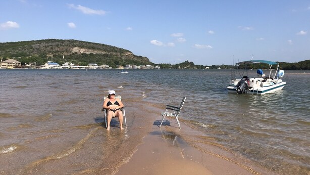 Una playa con agua cristalina, una mujer en traje de baño y un bote al fondo.