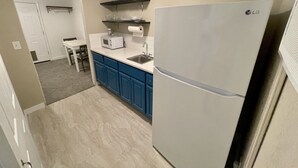 Una cocina compacta con un refrigerador blanco LG, armarios azules, un microondas y un pequeño lavabo en la encimera.