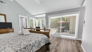Un dormitorio con una cama grande, un televisor sobre una cómoda y una puerta corrediza de vidrio que da a un espacio al aire libre con una mesa y sillas.