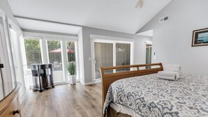 Un dormitorio con una cama de madera, una mesita de noche, una planta en maceta y un ventanal corredero que da a un balcón.