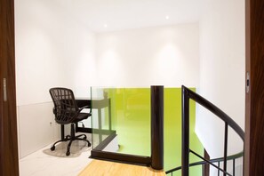 Een moderne kantoorruimte met een glazen scheidingswand, een zwarte bureaustoel en een houten vloer.