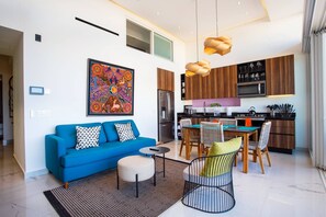 Un espace de vie moderne comprenant un canapé bleu, un coin repas et une cuisine dotée de meubles en bois et d’appareils électroménagers en acier inoxydable.