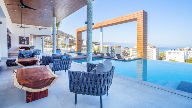Un espace de détente extérieur moderne, doté d’une piscine, de mobilier en bois et offrant une vue sur la ville.