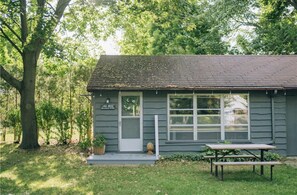 A small, single-story house with a porch, a sign reading "Lake House," and a picnic table in front.