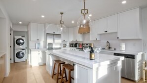 A modern kitchen with white cabinetry, a central island with stools, stainless steel appliances, and pendant lighting.