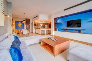 A modern living room with a sofa, coffee table, and a TV mounted on a blue accent wall. - Mamitas Beach & 5th Ave, Private Pool, Patio, Gym (Playa del Carmen)