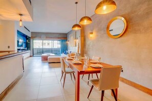 Uma sala de jantar com uma mesa comprida posta para quatro, área de cozinha com design moderno e uma janela grande que oferece iluminação natural.