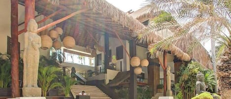 A modern building with a thatched roof, palm trees, and a staircase leading to an upper level.