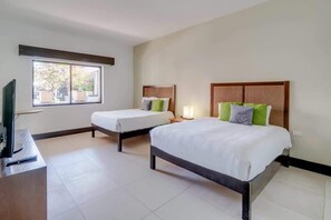 A hotel room with two beds, a television on a stand, and a window with a view of trees. - Mamitas Beach & 5th Ave, Private Pool, Patio, Gym (Playa del Carmen)