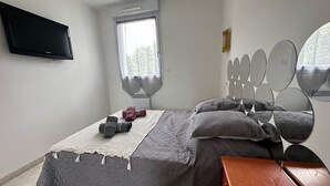 Un dormitorio con cama, televisión, ventana y espejo.