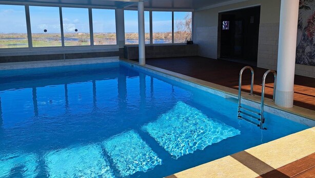 Una piscina interior con agua cristalina azul, grandes ventanales y vistas al paisaje.