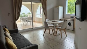 Un espacio habitable compacto con sofá, mesa de comedor, sillas, lavadora y televisor.