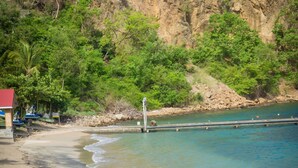 Une plage à l’eau claire, avec un rivage sablonneux et une falaise rocheuse.