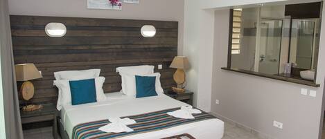 A hotel room with a wooden headboard, two bedside tables with lamps, a large bed with a striped bedspread, and a mirror above the bed.