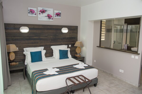 Una habitación de hotel con cabecera de madera, dos mesitas de noche con lámparas, una cama grande con colcha a rayas y un espejo sobre la cama.