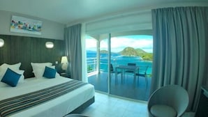 Une chambre d’hôtel comprenant un lit, un coin salon avec une table et des chaises, et un balcon avec vue sur la mer.