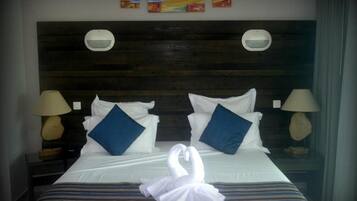A hotel room with a wooden headboard, two wall-mounted lamps, a bed with white bedding and blue pillows, and a swan-shaped decoration on the bed.