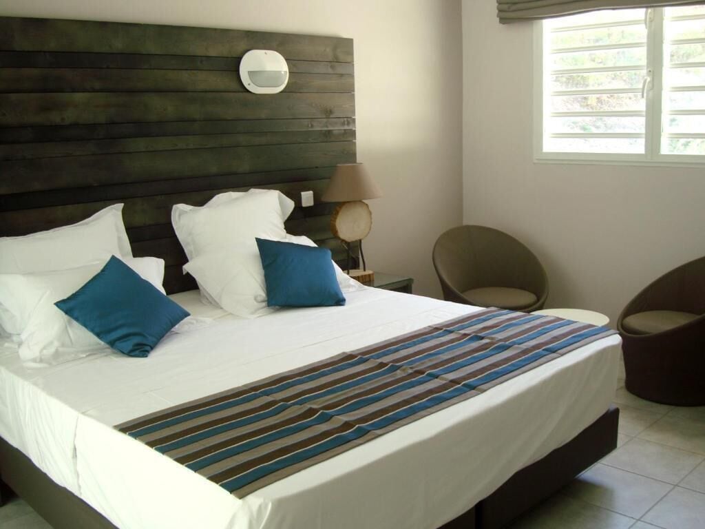A hotel room with a large bed, a round mirror on the headboard, a lamp, and a chair.