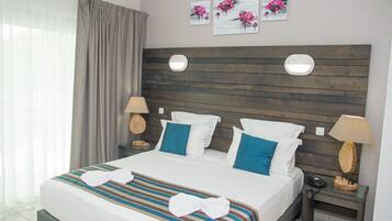 Un lit bien fait, avec une literie à rayures et des coussins bleus, une tête de lit en bois, deux tables de chevet avec des lampes et des œuvres d’art accrochées au mur.