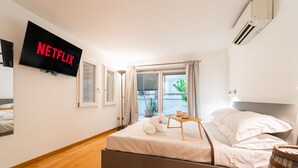 Ein modernes Hotelzimmer mit Bett, Nachttisch, Wandfernseher und einem Fenster mit Vorhängen.