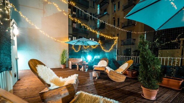 Eine Holzterrasse mit Sitzgelegenheit im Freien, Lichterketten und einem Blumentopf-Baum.