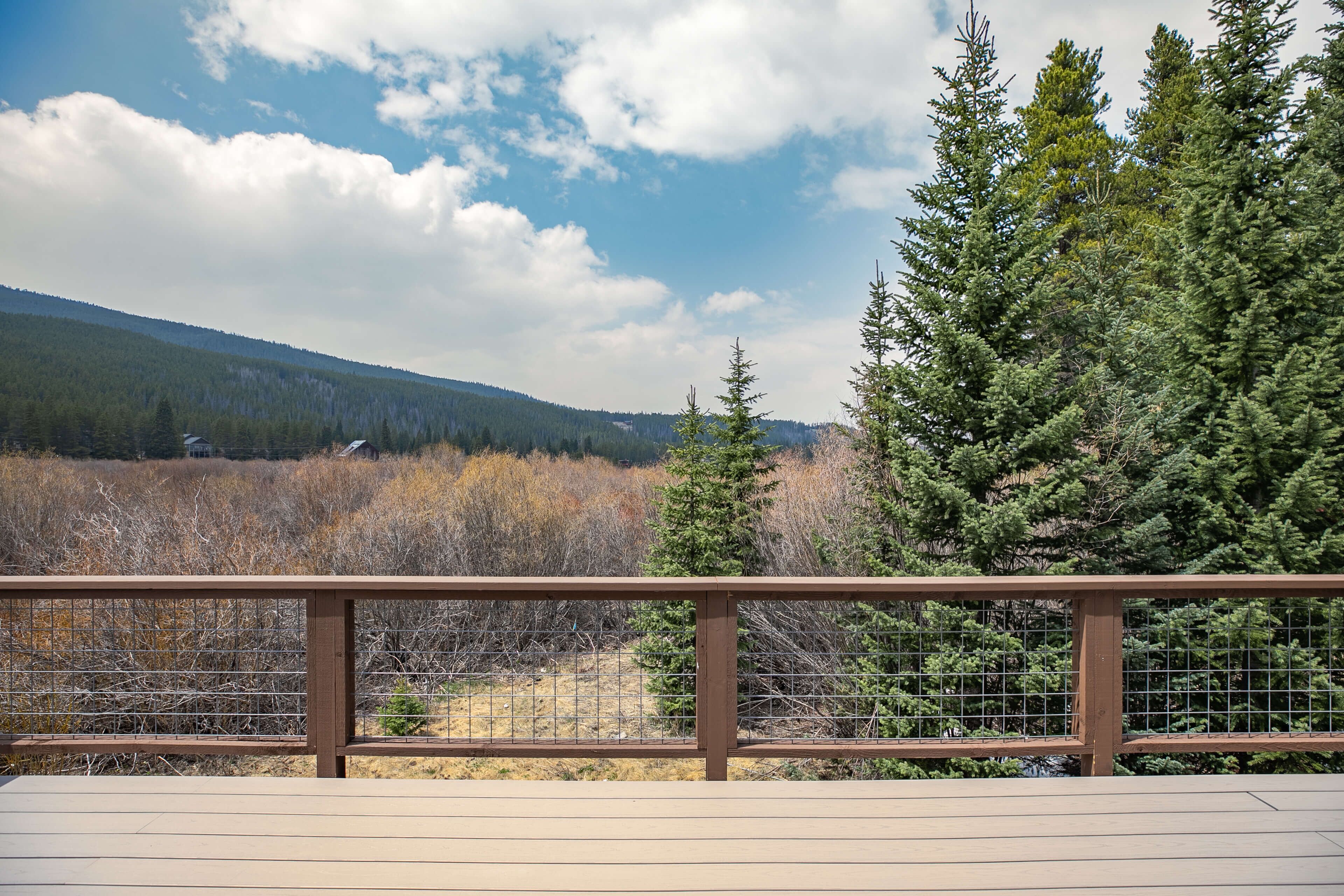 A wooden deck with a metal railing overlooking a forested area with mountains in the distance.