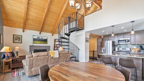 A spacious living room with a wooden dining table, a sofa, and a fireplace. A spiral staircase leads to an upper level. - The Fishermen’s Place: Mountain Views + Dog Friendly (Breckenridge)