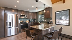 A modern kitchen with stainless steel appliances, a large island with bar stools, and a view of a snowy landscape through a window. - The Fishermen’s Place: Mountain Views + Dog Friendly (Breckenridge)