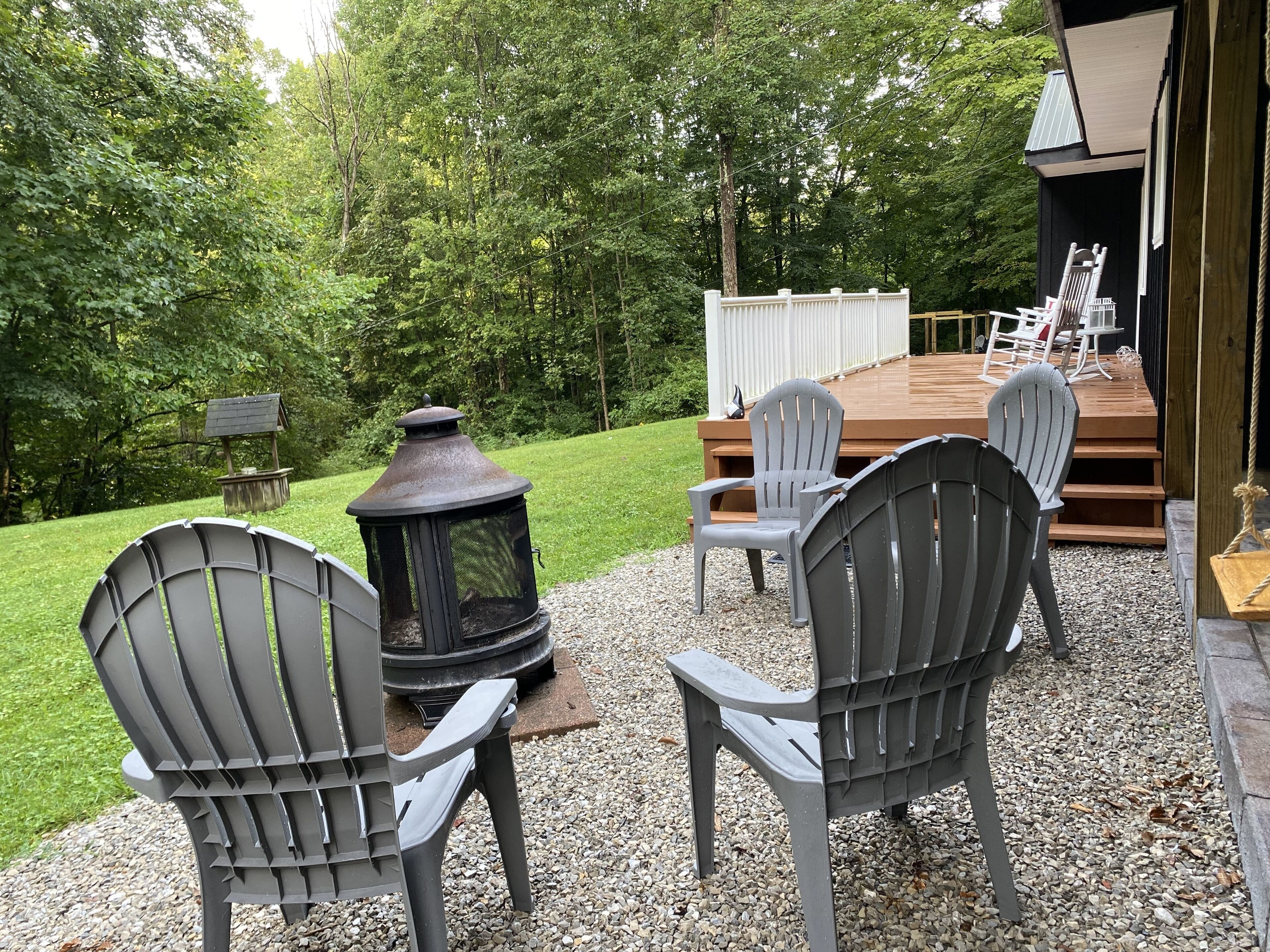 A deck with Adirondack chairs, a wood-burning stove, and a bird feeder.