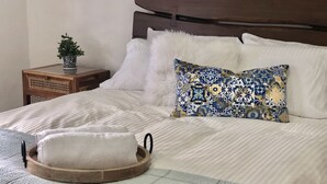 Un lit bien fait, avec une tête de lit en bois, des oreillers blancs et un coussin décoratif aux motifs bleus et jaunes.