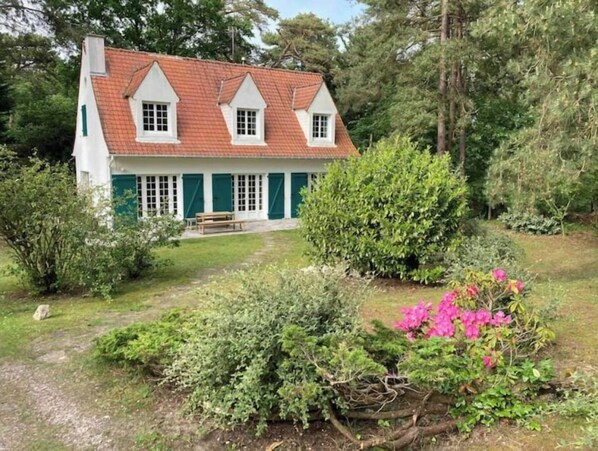 A traditional house with a sloped roof, green shutters, and a bench in front.