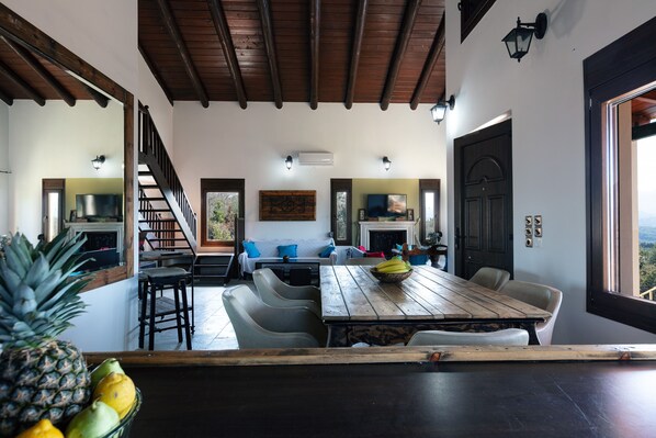 A dining area with a wooden table, chairs, and a fruit bowl. A staircase leads to another room.