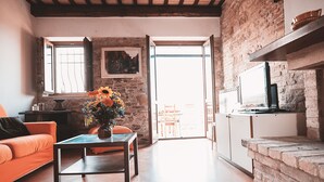 Una sala de estar con un sofá, una mesa de centro con un florero, un televisor sobre un mueble bajo y una pared de ladrillo.