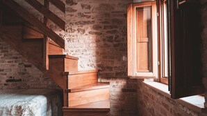 Una escalera de madera que lleva a una habitación con pared de piedra y una ventana con contraventanas de madera.