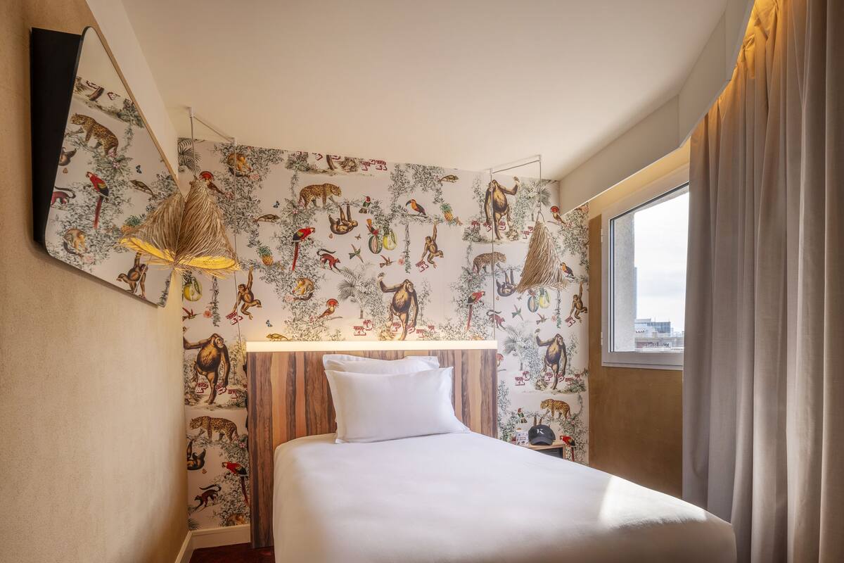 Een hotelkamer met een bed, een hanglamp en een muurschildering met dierenillustraties.